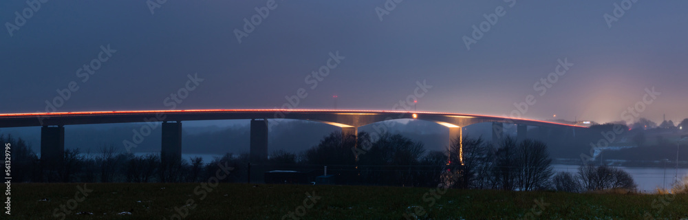Landscape view of traffic on the illuminated highway Alssundbroen (high car bridge over Alssund north of Sønderborg, Denmark) covered in fog. Long-exposure shot at night.
