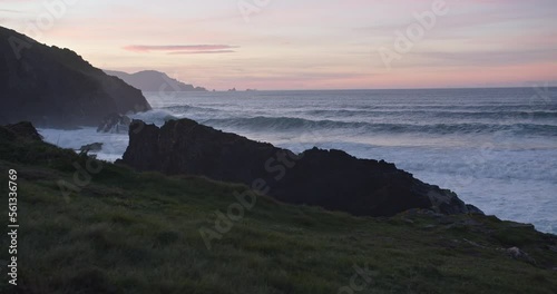 Big waves rolling into a deserted bay after sunset during blue hour in Galicia, Spain