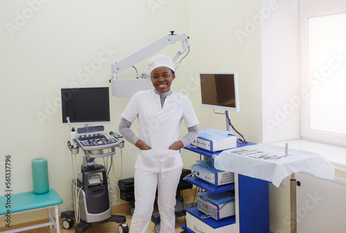 An African-American female doctor in a white coat stands in the treatment room.