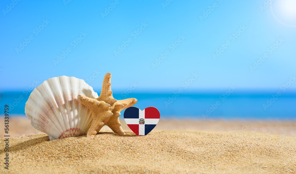 Beautiful beach in the Dominican Republic. Flag of Dominican Republic in the shape of a heart and shells on a sandy beach. - obrazy, fototapety, plakaty 