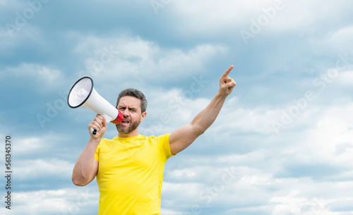 man in yellow shirt shout in megaphone on sky background with copy space