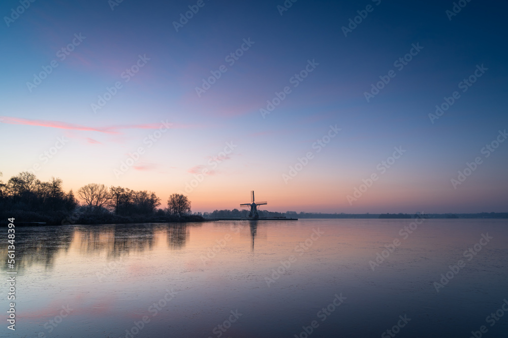 Colourful dawn over a frozen lake with a windmill.