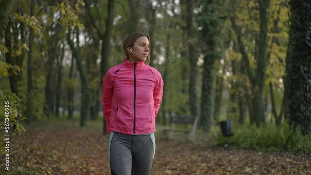Front view of a young woman wearing pink tracksuit walking and stretching her hands in an autumn forest at sunset in slow-motion Front view of a young woman wearing pink tracksuit walking and stretching her hands in an autumn forest at sunset in slow-motion