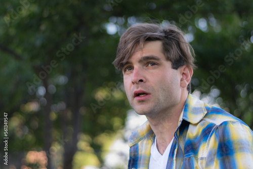 A young white man outdoors in a shady backyard setting with a serious expression.