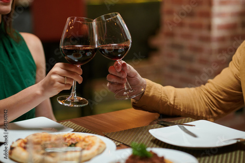 Couple clinking glasses of wine over dinner table in restaurant