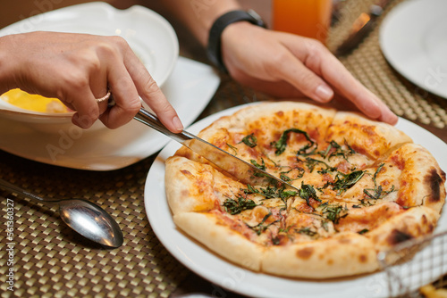 Hands of woman cutting small pizza she ordered in restaurant