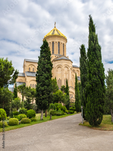 Tsminda Sameba or Holy Trinity Cathedral of Tbilisi, Georgia. Modern religious complex of Georgian Orthodox church with with golden dome surrounded by cypress trees in neat garden