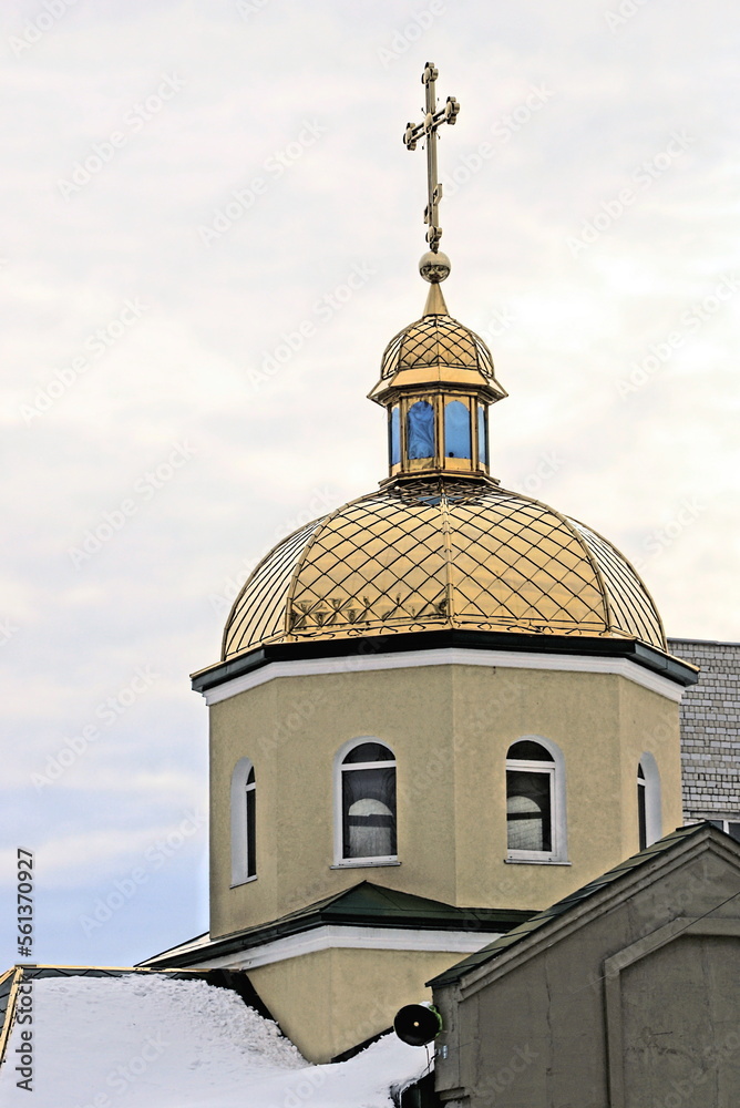 one brown stone church tower with small windows under a golden dome with a cross under white snow outdoors against a gray sky