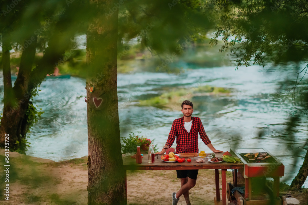 A man preparing a delicious dinner for his friends who are having fun by the river in nature A man preparing a delicious dinner for his friends who are having fun by the river in nature