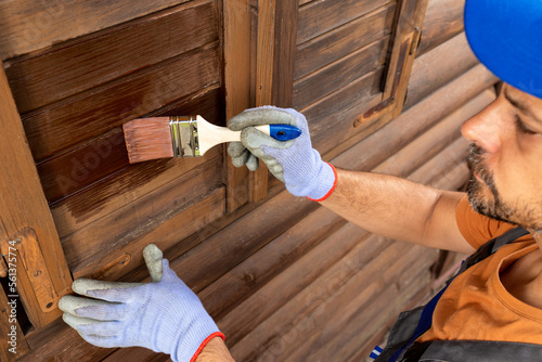Foto Worker applying protective varnish or wood oil on wooden house cottage exterior