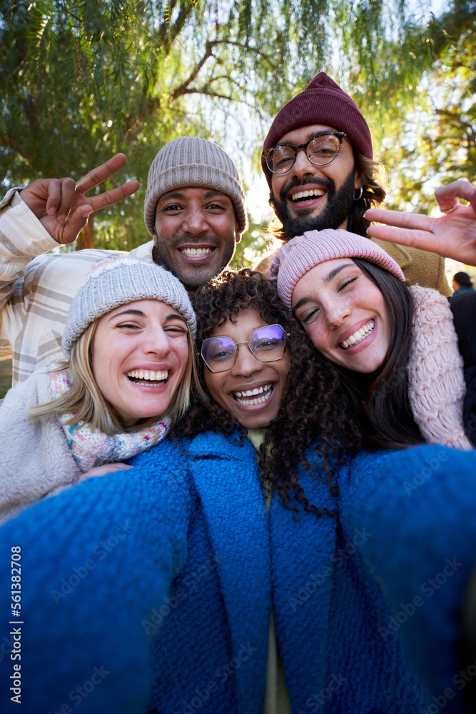 Vertical Winter time smiling selfie of a happy group of multicultural friends looking camera. Portrait of cheerful multi-ethnic young people of diverse races having fun together. Colleague hanging out