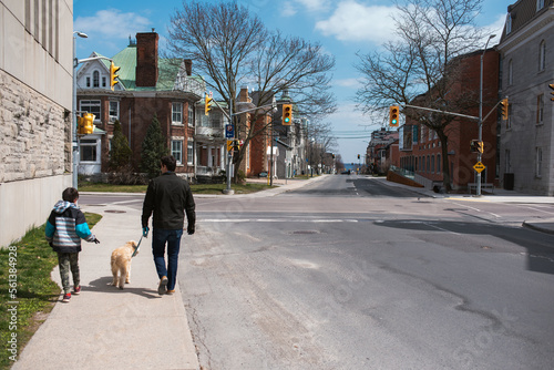 Father and son walking a dog on the sidewalk of a quiet city street. photo