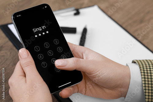 Woman unlocking smartphone with blocked screen at wooden table, closeup