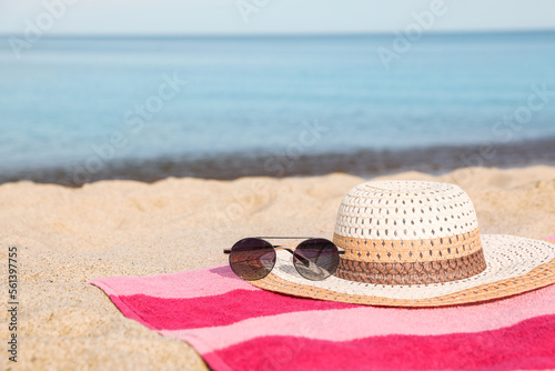 Beach towel with straw hat and sunglasses on sand near sea. Space for text