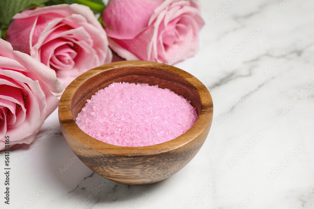 Wooden bowl with pink sea salt and beautiful roses on white marble table Wooden bowl with pink sea salt and beautiful roses on white marble table
