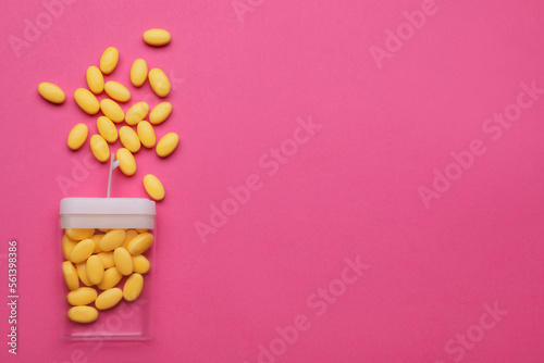 Tasty yellow dragee candies and container on pink background, flat lay. Space for text