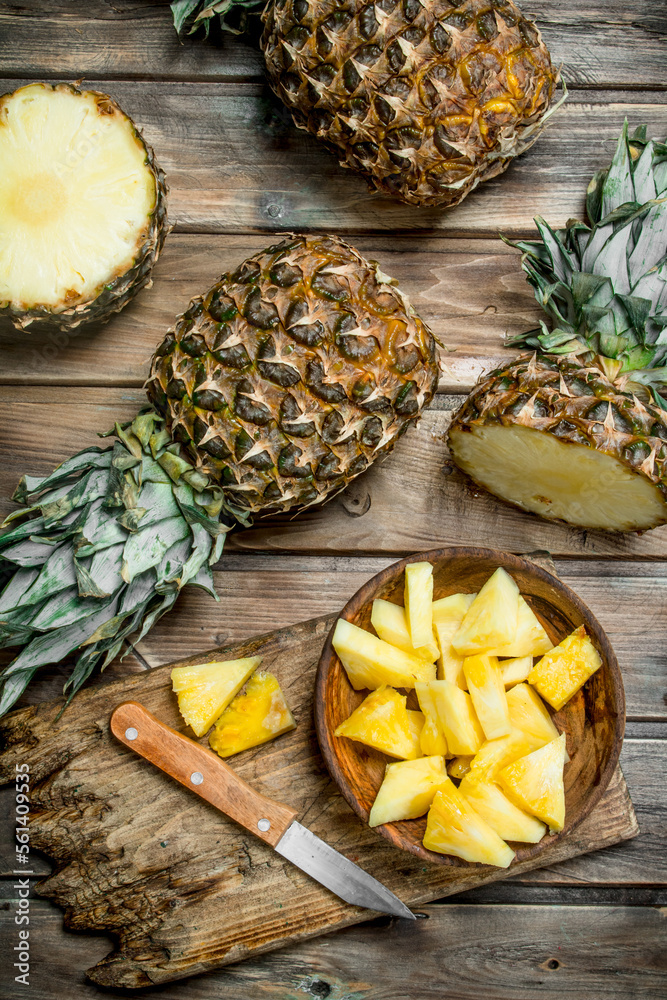 Fototapeta premium Sliced pineapple in a bowl on a cutting Board with a knife and a whole pineapple.