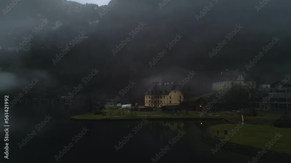 Aerial view of alpine village within mountainous landscape covered with dense, deciduous forest. Foggy skyline floating above the valley with a charming settlement around. High quality 4k footage Aerial view of alpine village within mountainous landscape covered with dense, deciduous forest. Foggy skyline floating above the valley with a charming settlement around. High quality 4k footage