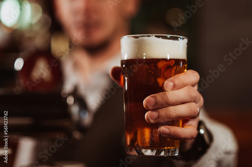 bartender s hand with a glass of light draft beer with foam in bar close-up