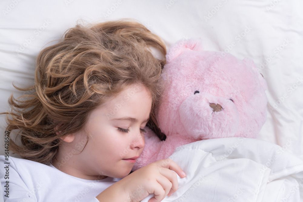 Cute child sleeping with a toy teddy bear on bed at home. Bedtime, kid