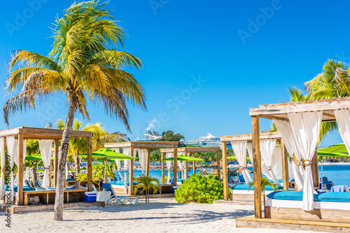 The paradise beach with cabanas  palms  and docked cruise ship