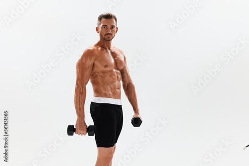 Man athletic body bodybuilder posing with dumbbells with naked torso abs full-length in the background, fitness class. Advertising, sports, active lifestyle, competition, challenge concept. 