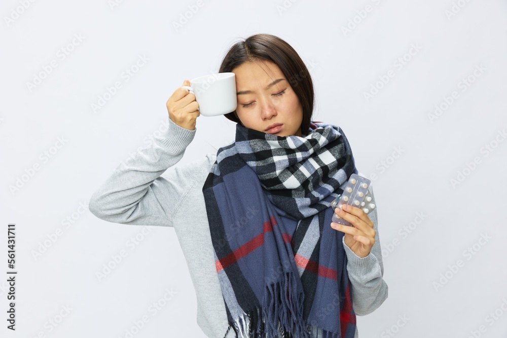 Asian woman cold flu holding a mug of medicine and pills in checkered plaid with fever is sick from the virus on a white background, copy space Asian woman cold flu holding a mug of medicine and pills in checkered plaid with fever is sick from the virus on a white background, copy space