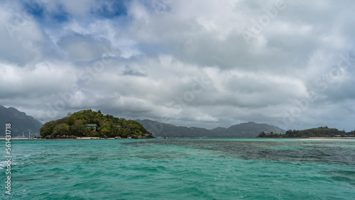 Small islands in the turquoise ocean are overgrown with tropical vegetation. Cottages are visible through the foliage of trees. The boats are moored at the shore. Clouds in the sky. Seychelles © Вера 