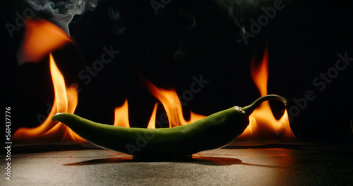 chili pepper green on fire, burning pepper, hot pepper, on a red and black background. hot pepper burn in the fire. 