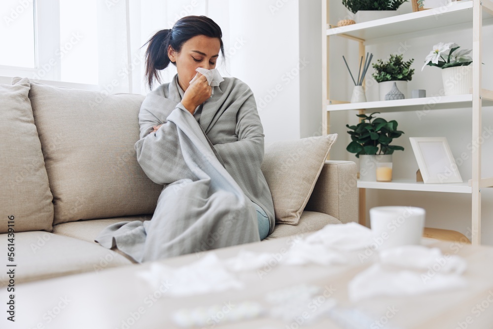 Woman cold headache runny nose and stuffy nose sitting on sofa in plaid, treatment for flu, allergies and covid-19 Woman cold headache runny nose and stuffy nose sitting on sofa in plaid, treatment for flu, allergies and covid-19
