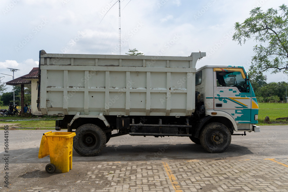 Logistics box truck is parked in city park near a yellow trash bin