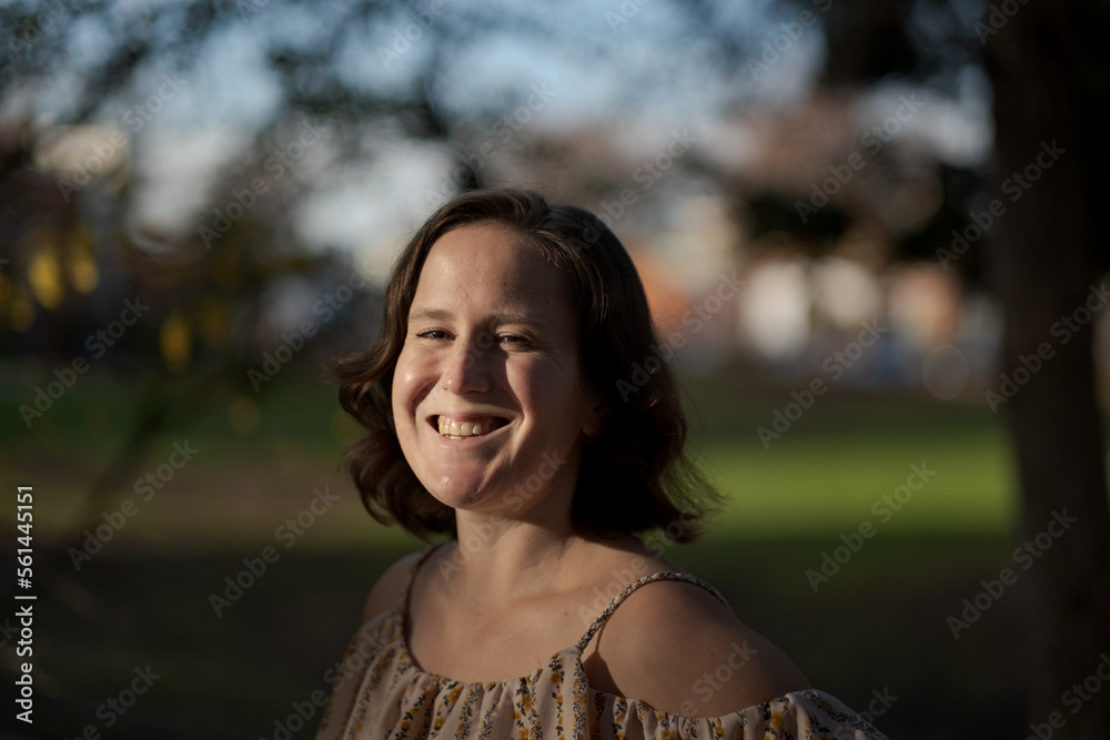A person wearing an open-shoulder blouse expresses themselves outdoors in a park setting.