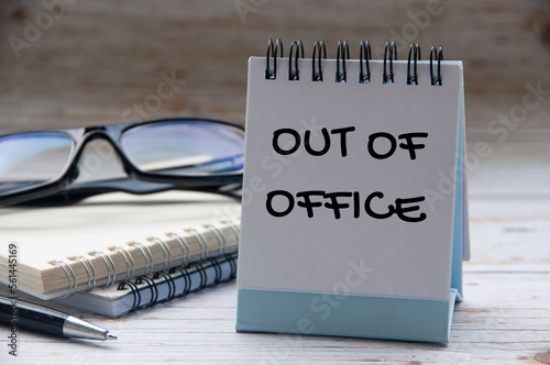 Out of office text on calendar desk with notebook and glasses background. Out of office concept.
