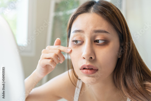Bored  insomnia asian young woman  girl looking at mirror hand touching under eyes with problem of black circles or panda puffy  swollen and wrinkle on face. Sleepless  sleepy healthcare person.
