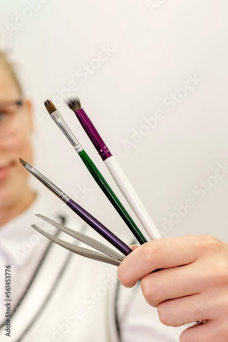 The master of eyebrows holds in his hands brushes for coloring hairs on a light background
