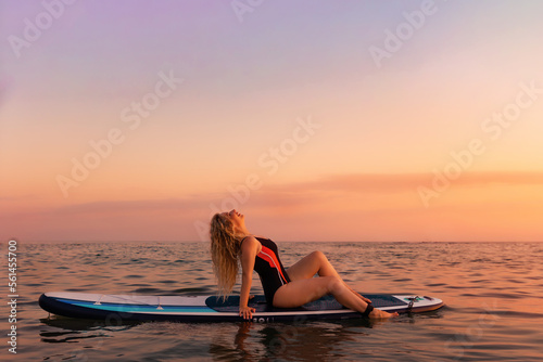 Summertime. Sexy young woman posing lying at sup board in the ocean. Copy space. Sunset at the background. The concept of sport and vacation © _KUBE_