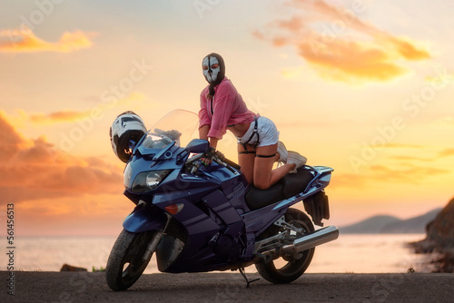 Fotografie, Obraz Sexy woman in a balaclava with skull poses on a tourist motorcycle