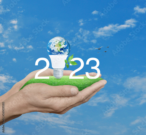 2023 white text and earth globe inside led light bulb with leaves on grass in hands over sky, Happy new year 2023 green ecology and saving energy concept, Elements of this image furnished by NASA