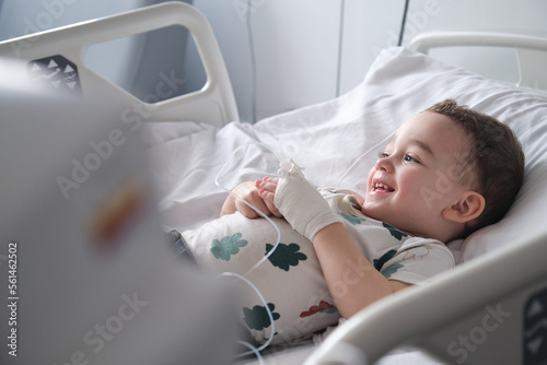 little boy in hospital lying in bed with an intravenous line in his hand smiling