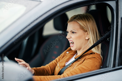 An angry blond woman is driving her car and honking at other drivers.