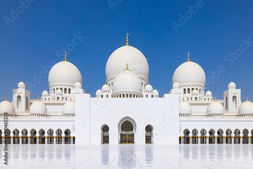Symmetrical close up of the main courtyard of the Sheik Zayed grand mosque in Abu Dhabi with the prayer hall and its round domes against a blue sky