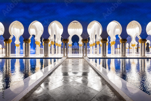 Symmetrical nightshot of the colonnade of the Sheik Zhayed mosque, with a marble catwalk surrounded by water