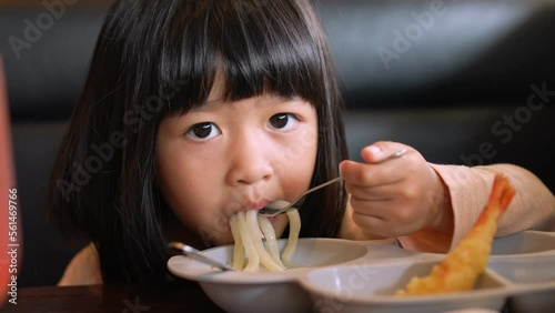 Asian girl sitting in the restaurant and eating Japanese noodles (Udon or ramen) and Shrimp Tempura with family and showing thumb up after eat.  Tasty is very delicious. Childhood, health concept.