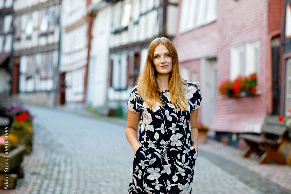 Beautiful young woman with long hairs in summer dress going for a walk in German city. Happy girl enjoying walking in cute small fachwerk town with old houses in Germany.