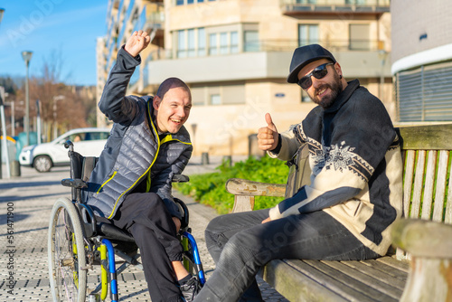 Portrait of disabled person in wheelchair with friend sitting having fun in the street © unai