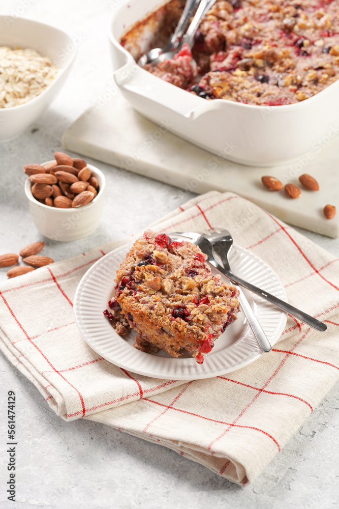 breakfast casserole idea - a piece of oven berry baked oatmeal with almonds, walnuts and coconut flakes on a white porcelain dessert plate on a checkered kitchen napkin