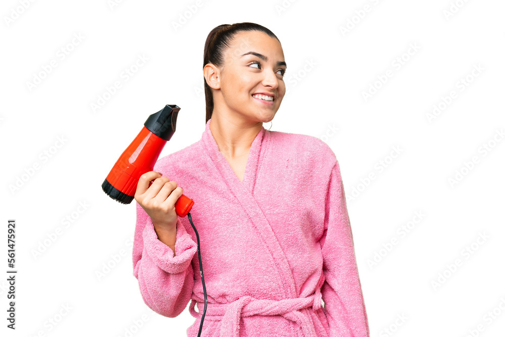 Young woman in a bathrobe holding a hairdryer over isolated chroma key background looking up while smiling Young woman in a bathrobe holding a hairdryer over isolated chroma key background looking up while smiling