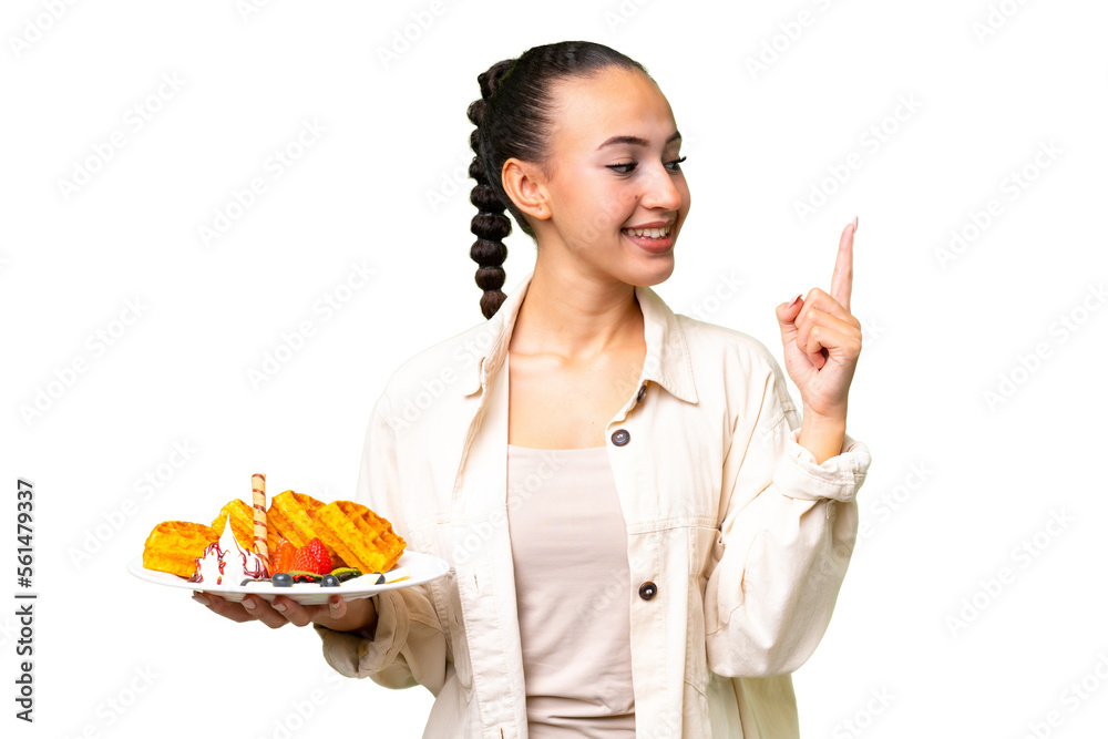 Young Arab woman holding waffles over isolated background pointing up a great idea Young Arab woman holding waffles over isolated background pointing up a great idea