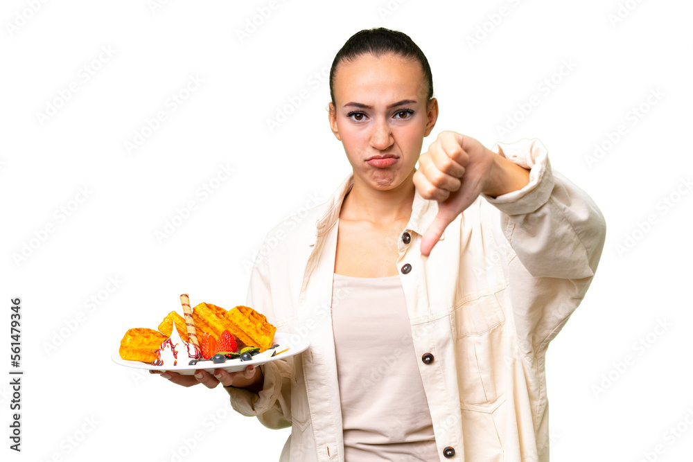 Young Arab woman holding waffles over isolated background showing thumb down with negative expression Young Arab woman holding waffles over isolated background showing thumb down with negative expression