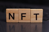 word NFT, non-fungible token made from wooden blocks on a laptop. The concept of earning on NFT